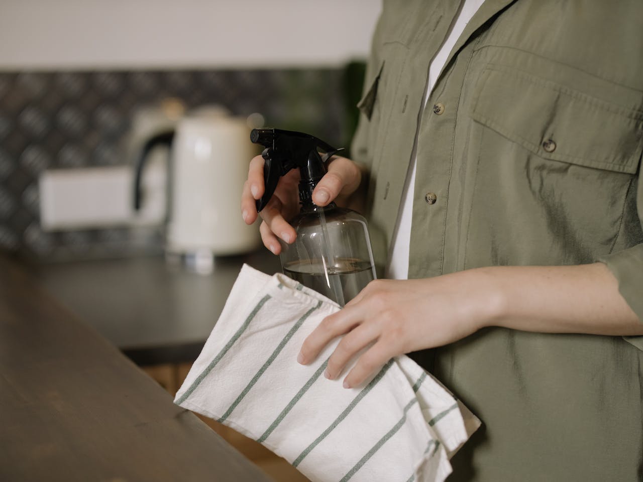 A person cleaning a kitchen counter with a spray bottle and cloth, maintaining cleanliness.